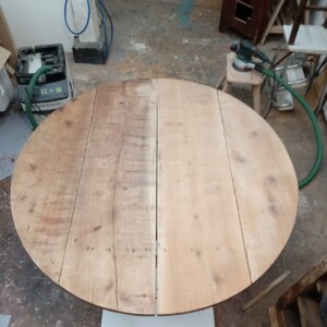 Ponçage d'une première moitié Restauration d'une table en noyer dans un atelier d'ébéniste et de menuisier à Paris, fait à la main, travail de finition, vernis, travail artisanal, travail du bois à Paris